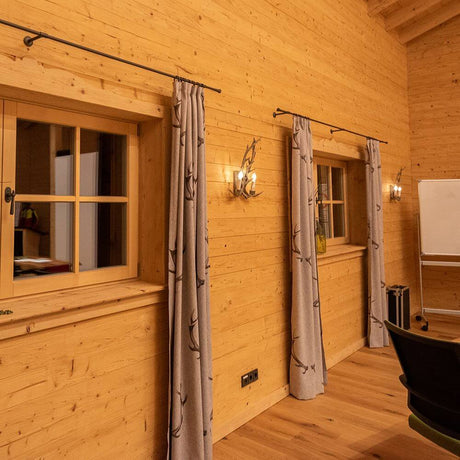Chalet Holz Geweih-Wandleuchte 2-flammig in einer gemütlichen Holzinnenausstattung mit Fenstern und Vorhängen.