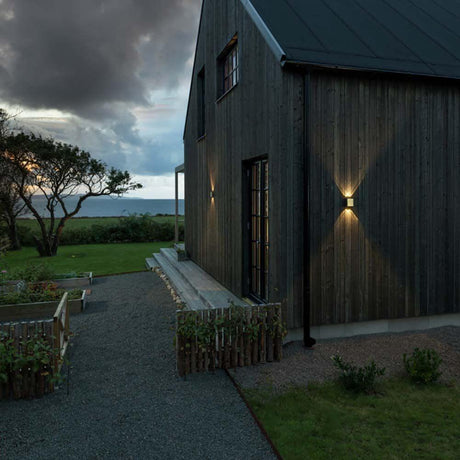 Chieri LED Wandleuchte Up & Downlights an einer modernen Holzfassade mit Gartenbeleuchtung.
