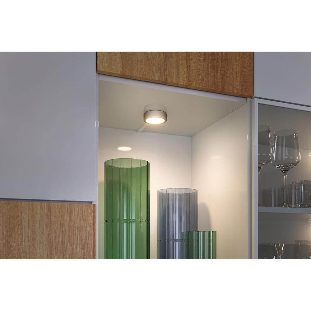 Clever LED Spot Disc CCT Weiß, Chrom-Matt in einem Schrank mit grünen und transparenten Gläsern.