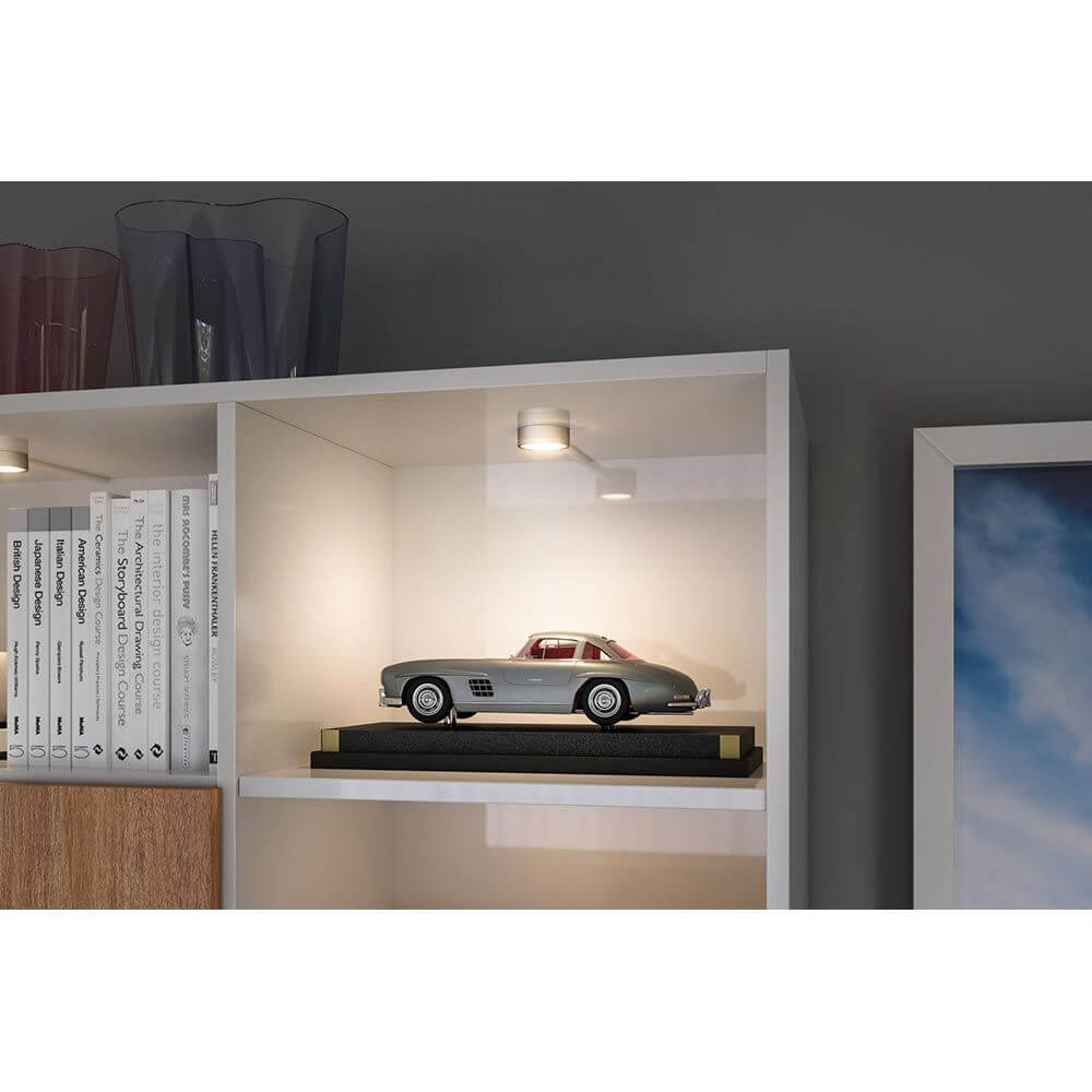 Clever LED Spot Medal CCT-Dimmbar Chrom beleuchtet eine Sammlung in einem modernen Regal.