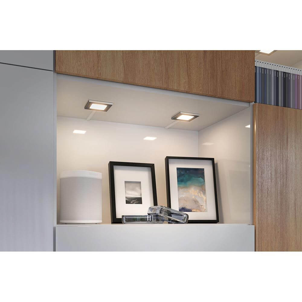 Clever LED Spot Pola CCT Weiß, Chrom-Matt sorgt für optimale Beleuchtung in Holzschrank mit Bildern und Lautsprecher.