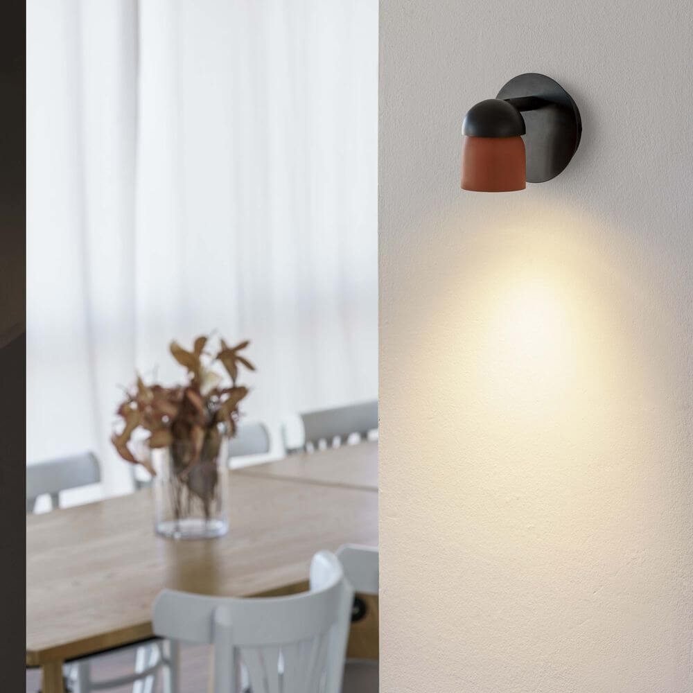 Coco Spot-Wandlampe an der Wand eines Essbereichs, warmes Licht auf einem Tisch mit Blumen.