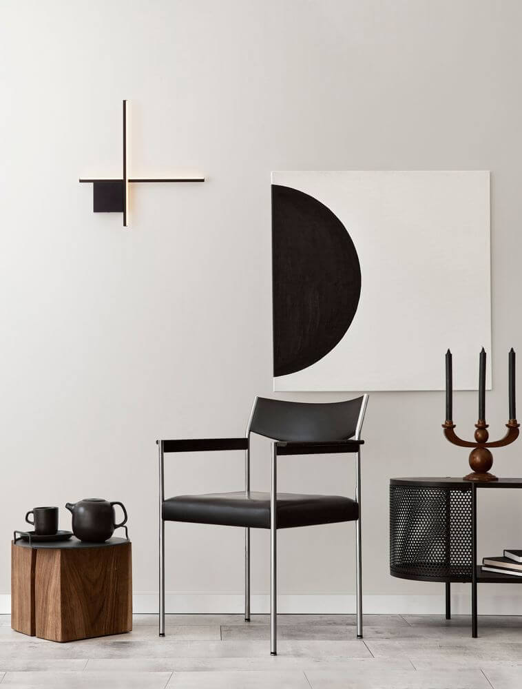 Elegante Cross LED Wandleuchte in mattem Gold, kombiniert mit modernem Stuhl und Kunstwerk für stilvolles Raumdesign.