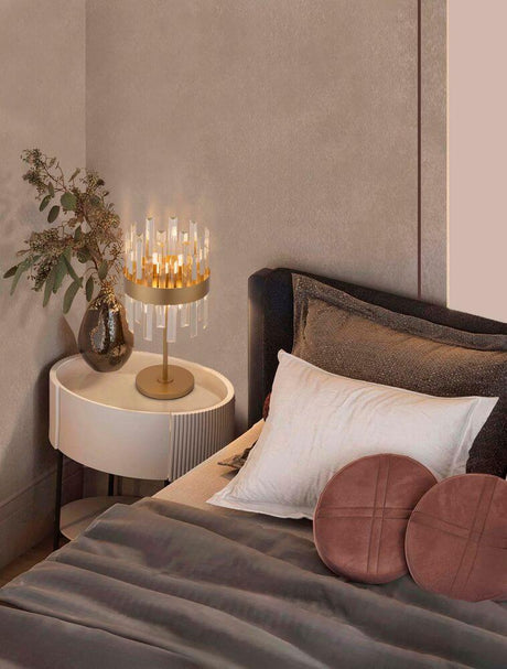 Lampe de table Crown Gold sur table de chevet à côté du lit, avec des coussins et une décoration élégants.
