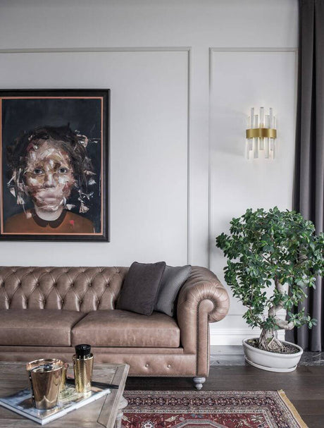 Crown wall light satin gold next to a brown Chesterfield sofa in a stylish living space.