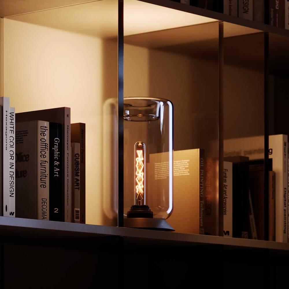 s.luce Cruet E27 Design Tischleuchte Glas mit Schalter auf Regal zwischen Büchern.