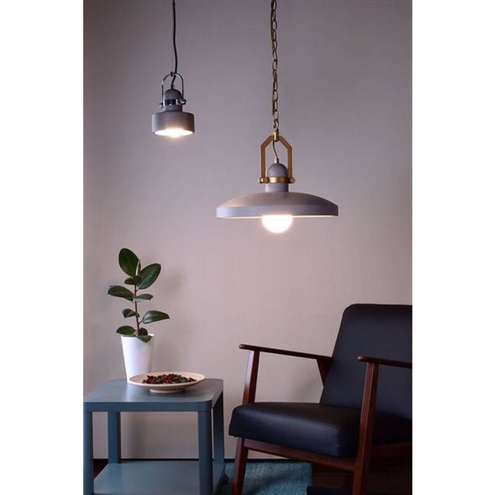 Pavo Betong-pendellampe Ø 14 cm i industrial-stil i en moderne stue med en plante og en lenestol.