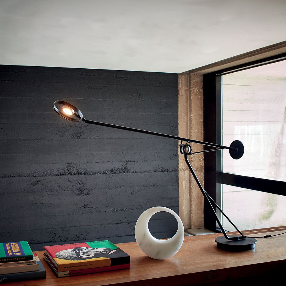 DCWéditions Aaro LED Tischleuchte in Schwarz auf einem Holzregal mit Büchern und einer modernen Skulptur.