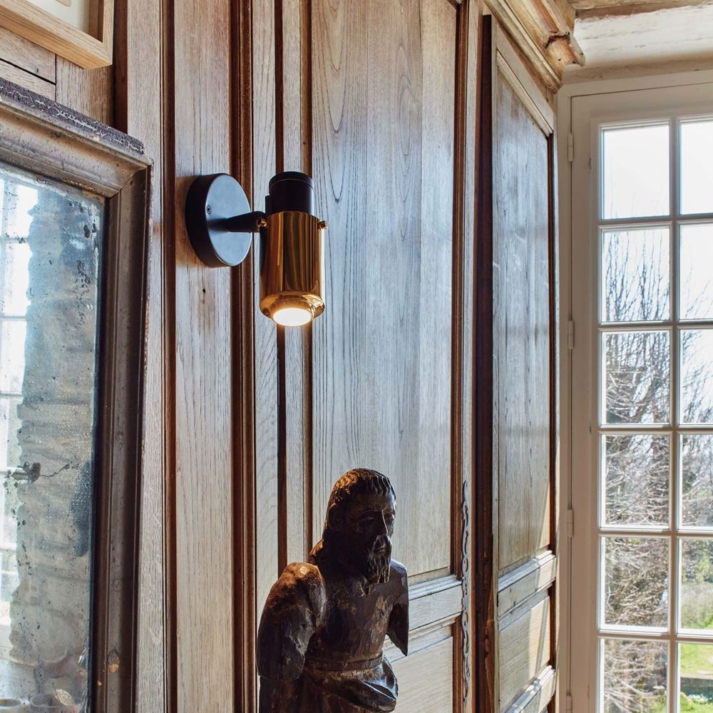 DCWéditions Biny Spot Wandleuchte in schwarz und messing an Holzwand, Lichtstrahl fokussiert auf Skulptur.