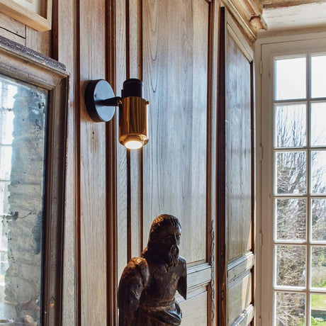 DCWéditions Biny Spot Wandleuchte verstellbar an Holzwand mit Statue im Vordergrund.