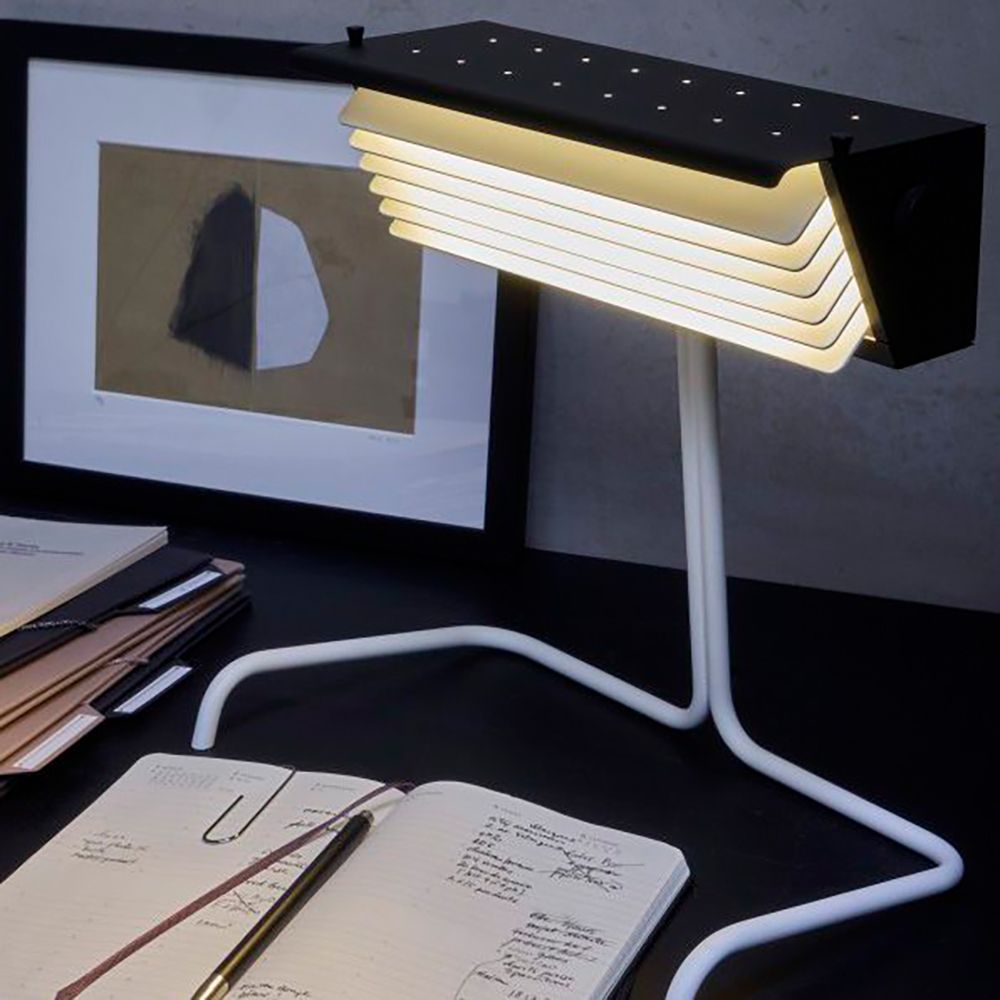 DCWéditions Biny Tischleuchte mit Lamellen auf einem Schreibtisch neben Schreibmaterialien