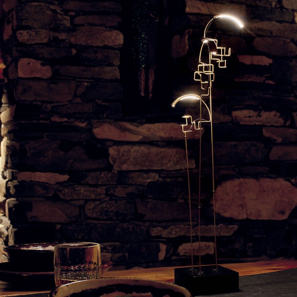 DCWéditions Boucle LED Akku Tischlampe schwarz Gold in gemütlicher Umgebung bei Nacht.