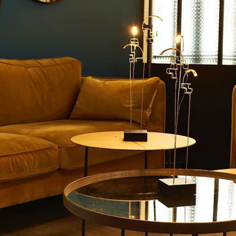 DCWéditions Boucle LED Akku Tischlampe schwarz Gold auf einem Tisch mit einem bequemen Sofa im Hintergrund.