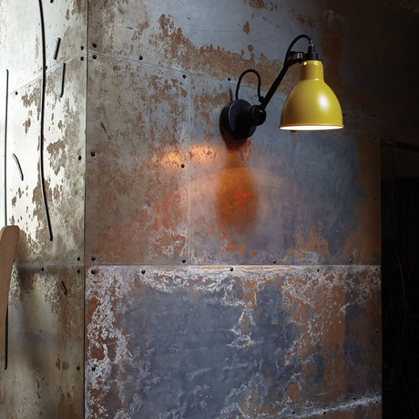 DCWéditions Gras N°304 Wandleuchte mit Schalter drehbar an einer Wand mit metallischen Oberflächen.