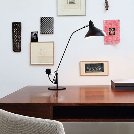 DCWéditions Mantis BS3 Retro Tischleuchte verstellbar auf einem modernen Schreibtisch mit Kunstwerken im Hintergrund.