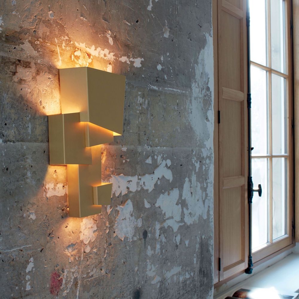 Geometrische Wandleuchte DCWéditions Map 1 in gold auf einem Betonwand mit natürlichem Licht.