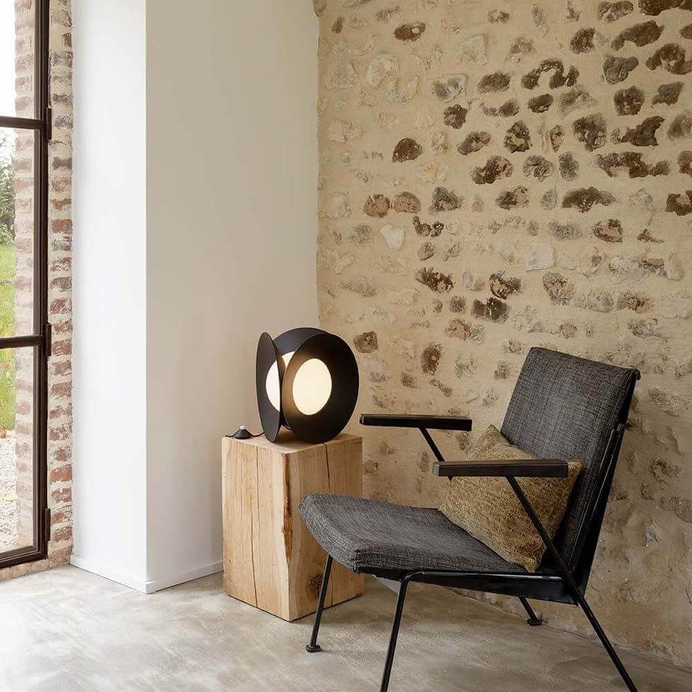 DCWéditions Armen LED Tischleuchte Matt-Schwarz neben einem Sessel in moderner Innenarchitektur.
