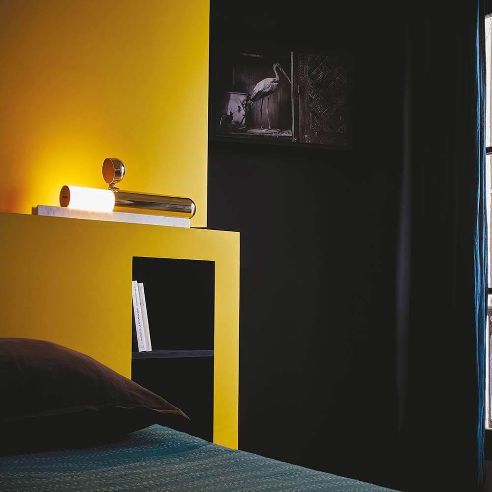 DCWéditions ISP LED Marmor Tischleuchte Messing-Lackiert auf Nachttisch mit gelber Wand im Schlafzimmer.