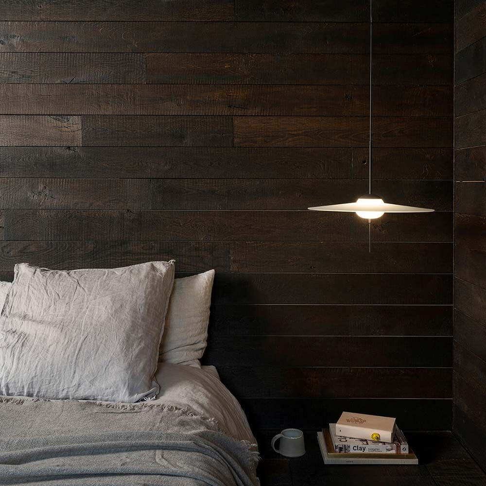 DCWéditions Mono LED Glas Hängeleuchte L über einem Bett mit einer Holzwand im Hintergrund.