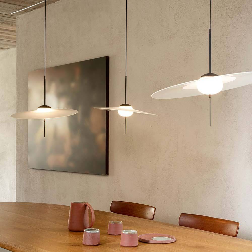 DCWéditions Mono LED Hängeleuchte M über einem Holztisch mit farbigen Gefäßen und Kunstwerk im Hintergrund.