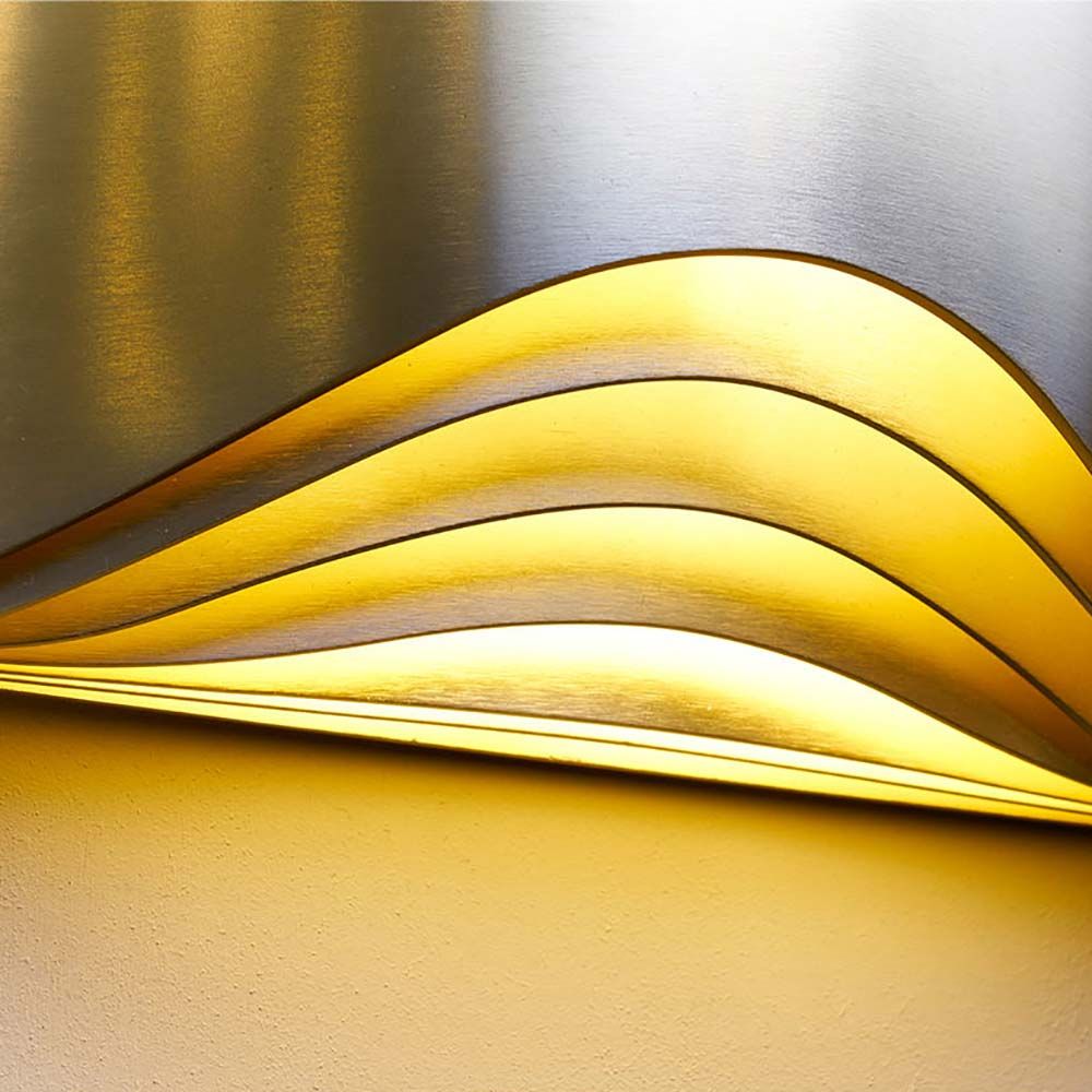 Elegante Wandleuchte Respiro von DCWéditions mit warmem, goldenem Licht und geschwungenem Design.