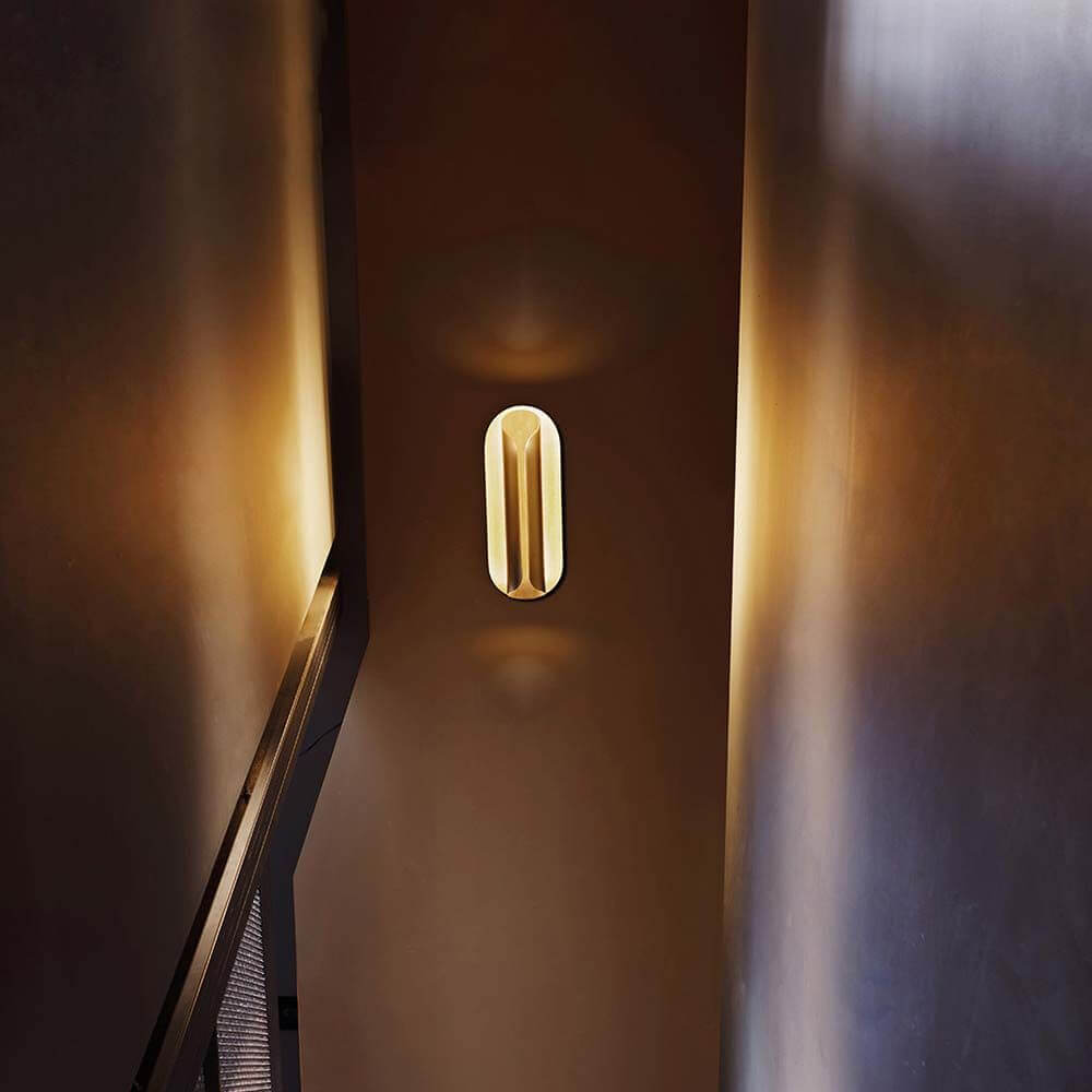 DCWéditions Rosalie LED Wandleuchte Blattgold an einer Wand mit warmem Licht in einem Treppenhaus