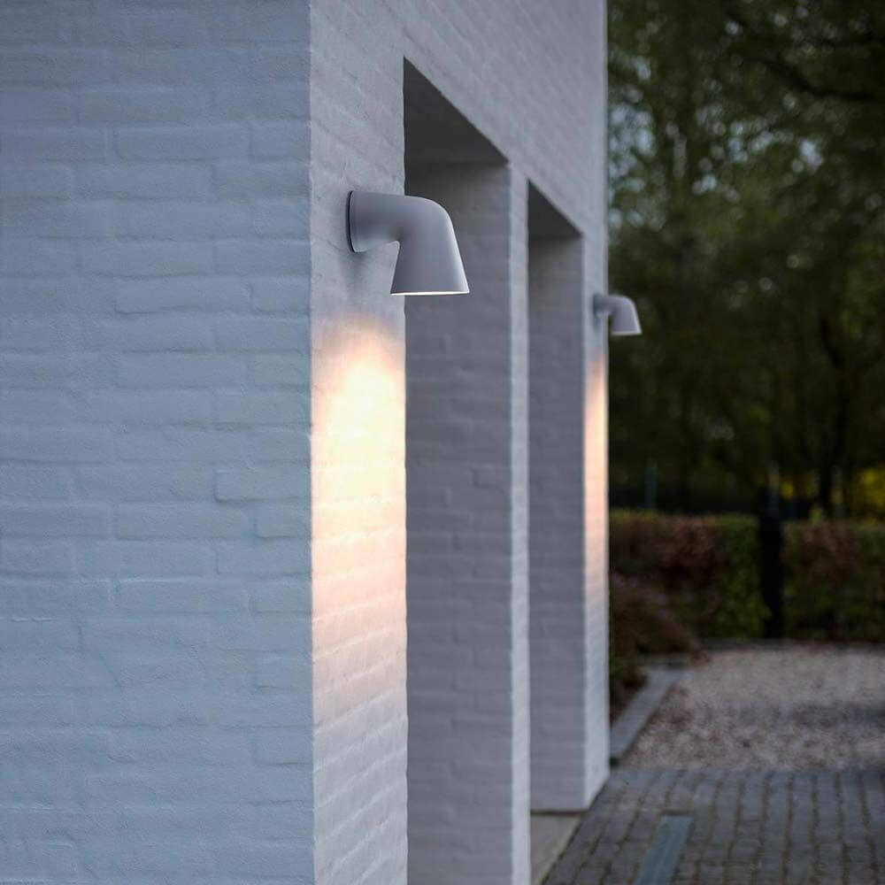 Außen-Wandleuchte Front Single IP44 Weiß an einer weißen Wand montiert, strahlt warmes Licht aus.