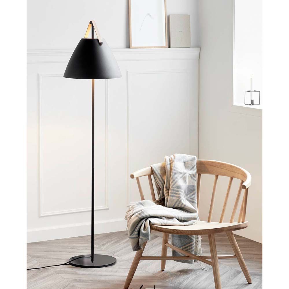 Stehlampe Strap Schwarz in modernem Interieur neben einem Holzstuhl mit Decke.