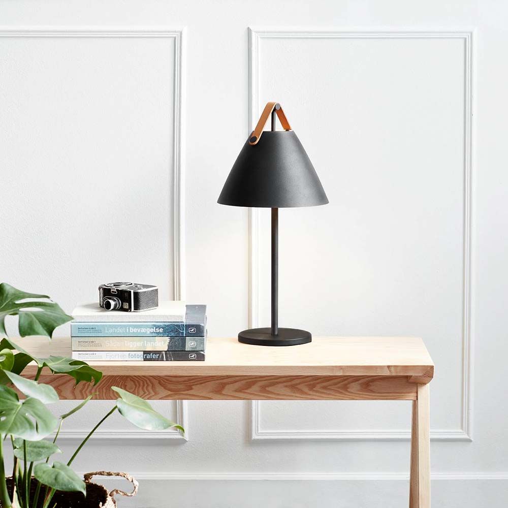 Tischlampe Strap Schwarz auf einem Holztisch mit Pflanzen und Büchern im modernen nordischen Stil.