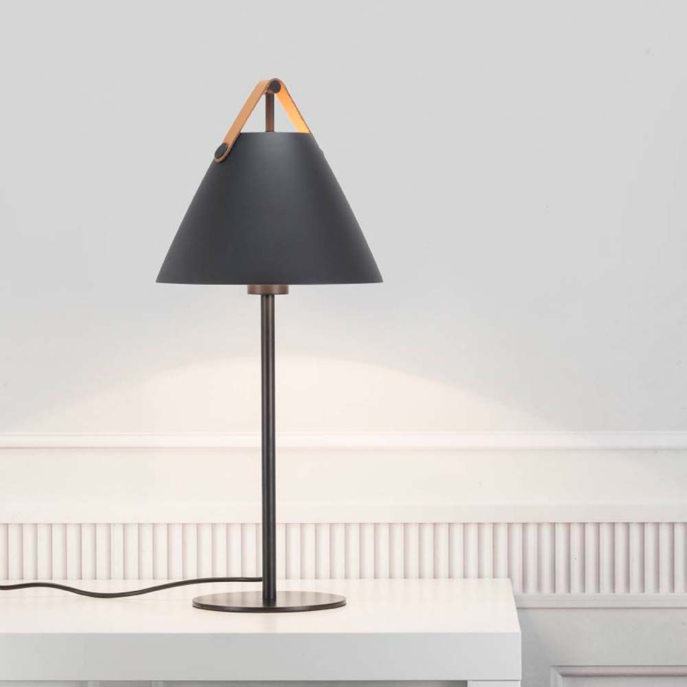 Tischlampe Strap Schwarz mit schwarzem Lampenschirm und Ledergriff auf einem Tisch.