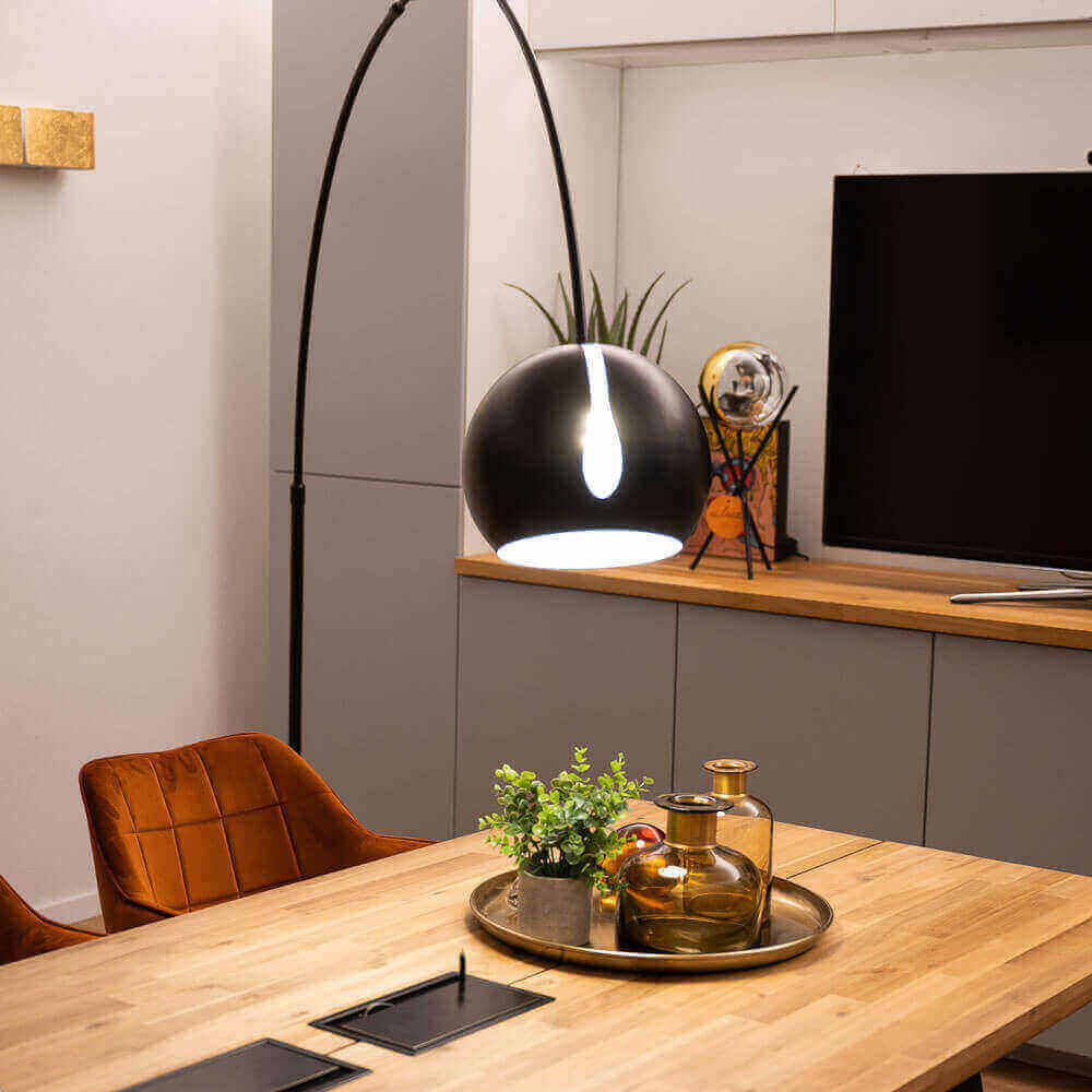 Moderne Esszimmerbeleuchtung mit schwarzer Pendelleuchte über einem Holztisch und stilvollem Geschirr.