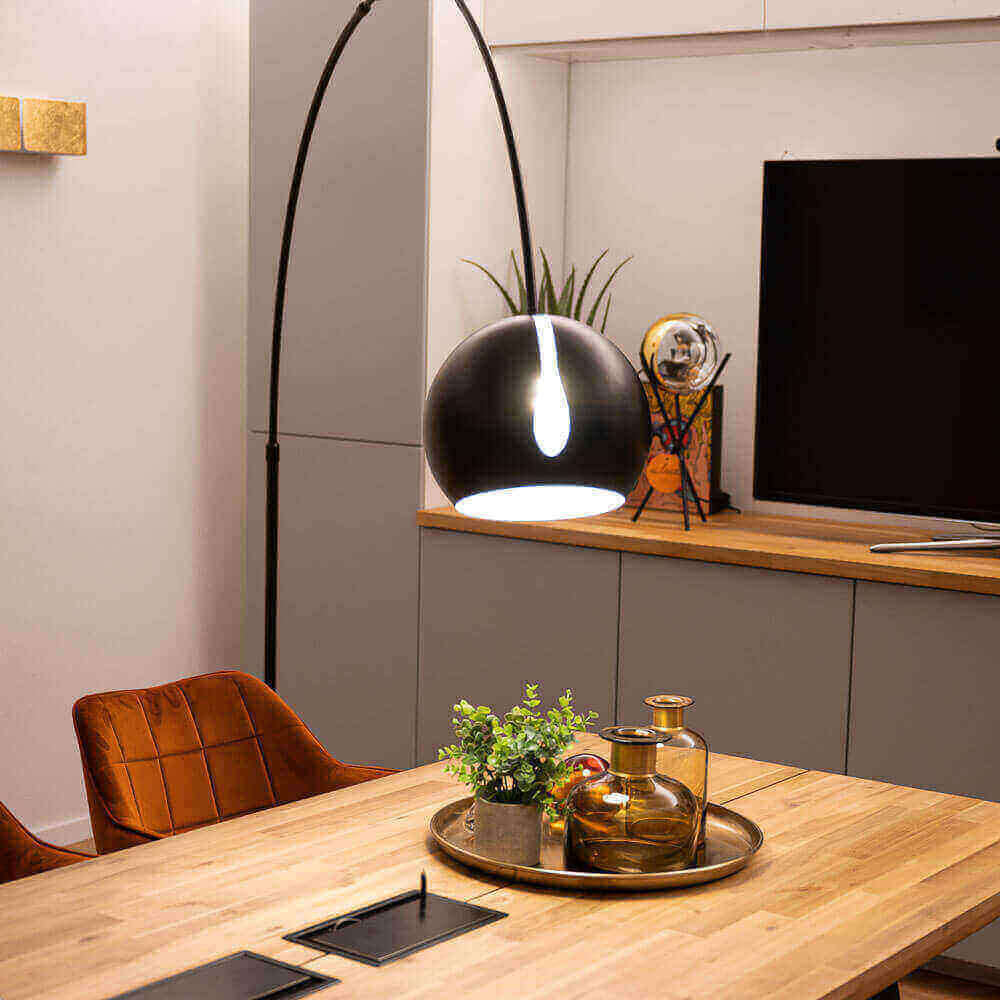 Moderne Esszimmerbeleuchtung mit schwarzer Pendelleuchte über einem Holztisch und stilvollem Geschirr.