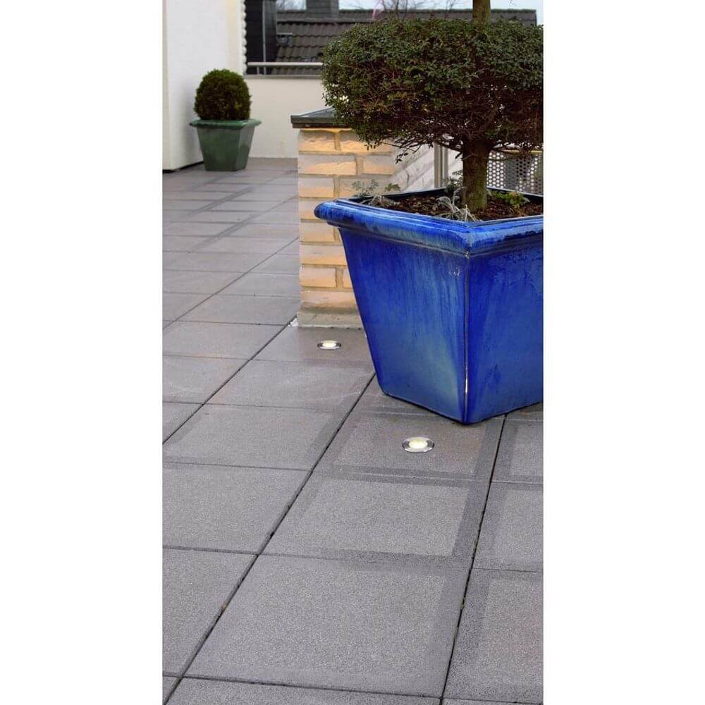 Runder Bodeneinbaustrahler im Außenbereich mit Edelstahlblende und blauer Pflanzgefäß auf Terrasse