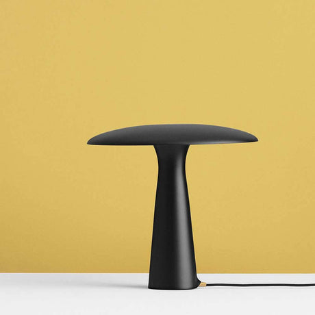 Lampada da tavolo di design Shelter Ø 41cm nera su tavolo bianco con sfondo giallo.