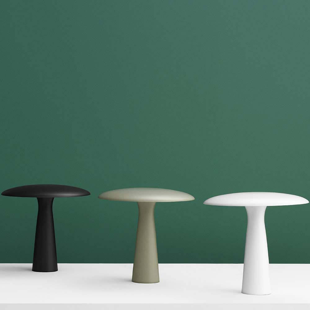 Design Tischleuchte Shelter in Schwarz, Oliv und Weiß vor grünem Hintergrund.