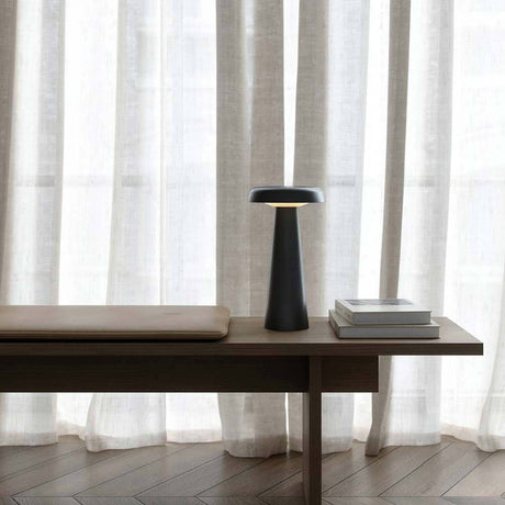 Arcello LED Außen Akku Tischleuchte auf einem Tisch neben einer Sitzbank und drei Büchern.