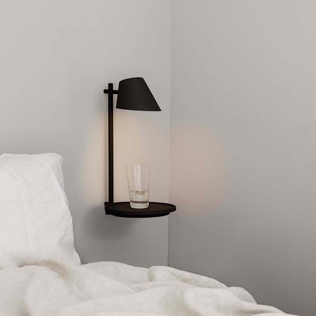 LED Wandleuchte Stay mit USB Schwarz an einer Wand neben einem Bett mit Glas auf dem Ablagebrett.