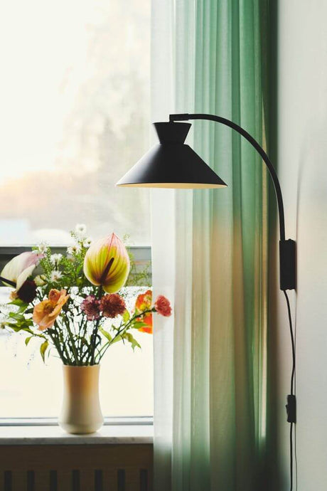 Dial wall light next to a flower vase with colorful flowers by the window.