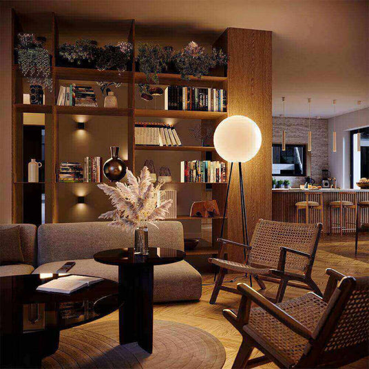 Modernes Wohnzimmer mit Bücherregal, Pflanzen, stilvoller Stehlampe und gemütlicher Sitzgelegenheit.