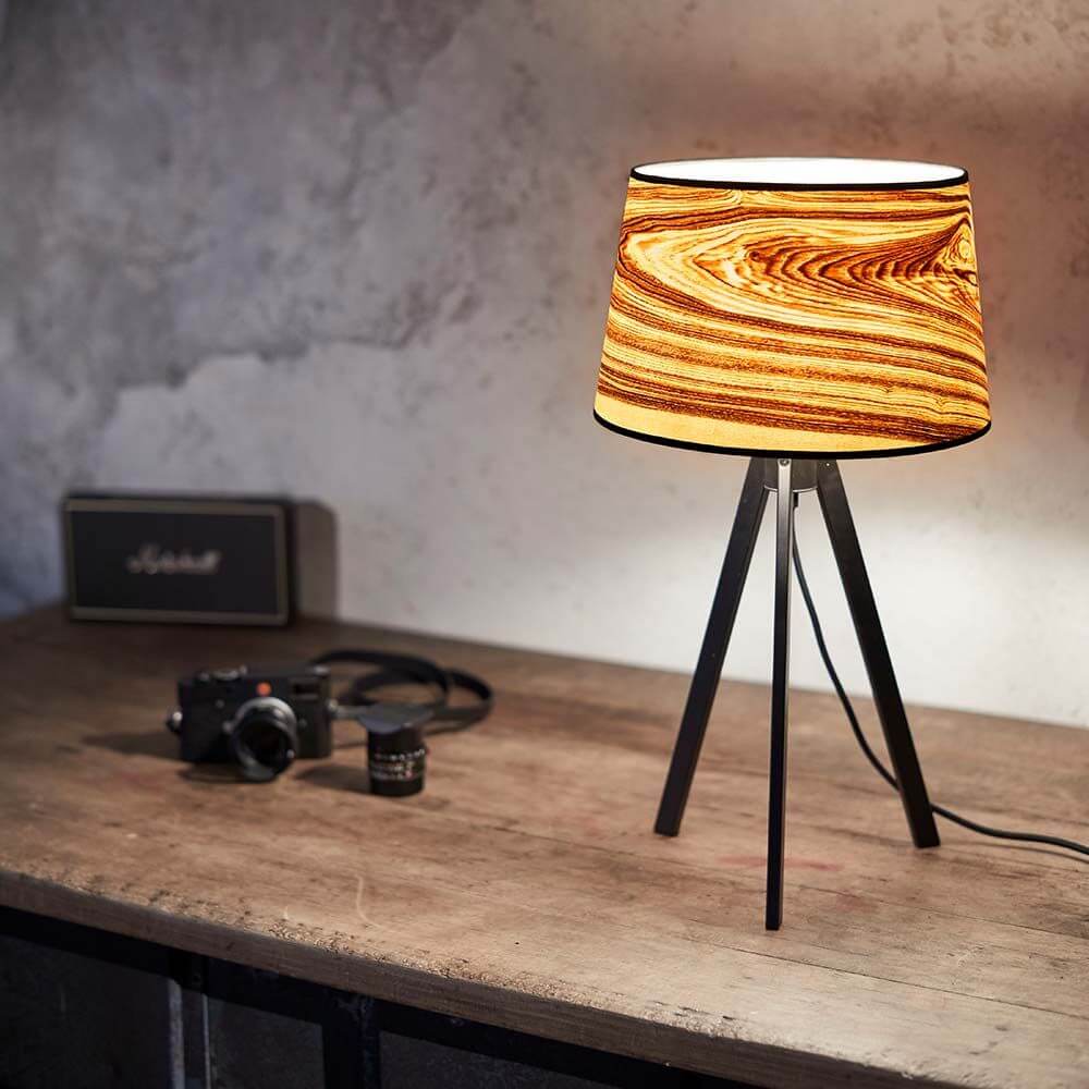 Dreibeintischlampe Attica 60cm Esche mit konischem Schirm aus Echtholzfurnier auf einem Tisch.