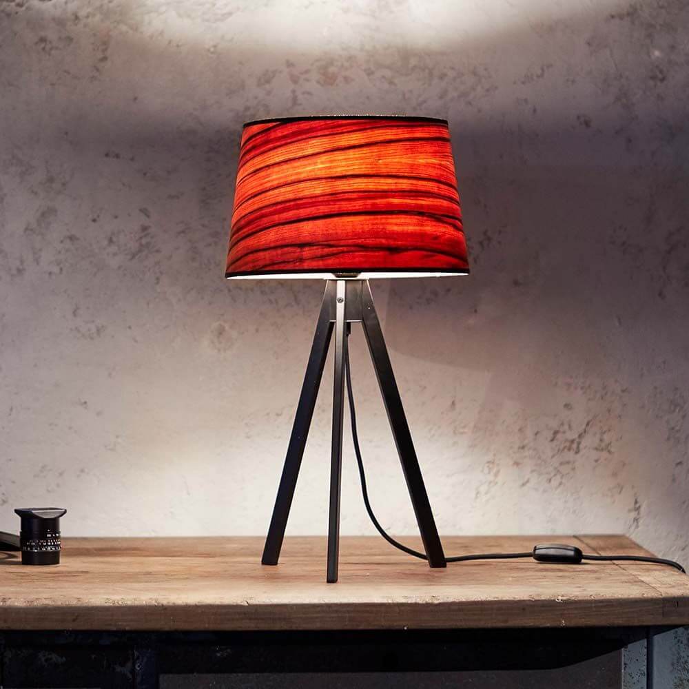Dreibeintischleuchte Attica mit konischem Schirm in rot und Holzfurnier auf einem Tisch, ideal für gemütliche Lichtinseln.
