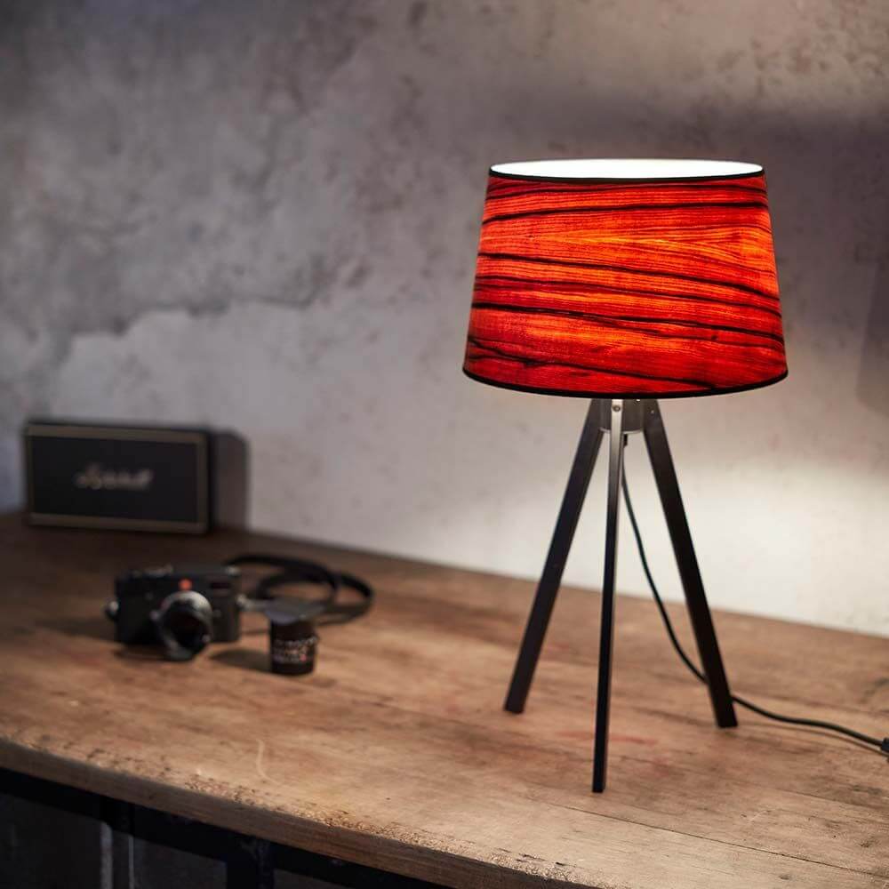 Dreibeintischleuchte Attica mit rotem Schirm auf einem Holztisch im modernen Raum.