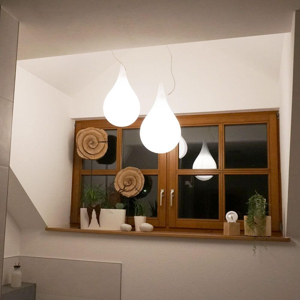 Drop-2S Pendelleuchte Ø 27cm Liquid-Light Weiß in stilvollem Innenraum mit Pflanzen und Holzfenster.