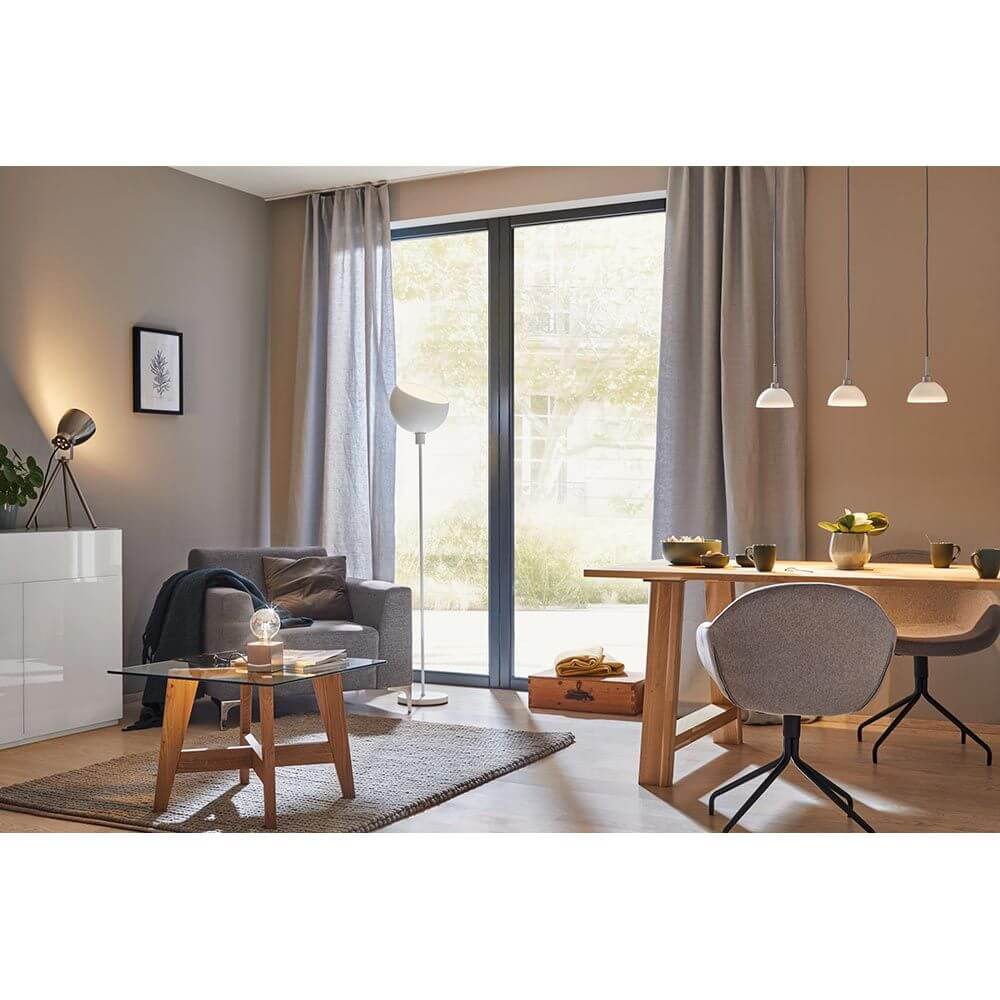 Gemütliches Wohnzimmer mit modernen Möbeln, Lampen und großen Fenstern im Tageslicht.