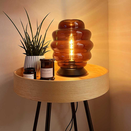 Moderne Tischlampe mit honeycomb-Design, Pflanzen und Duftkerzen auf einem Holztablett.