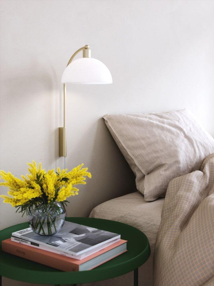 Ellen 20 Wandleuchte neben einem Bett mit Blumenvasen und Zeitschriften auf einem grünen Tisch.