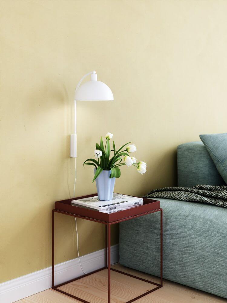 Ellen 20 Wandleuchte mit minimalistischen Design neben einem Tisch mit Blumen und Zeitschriften.
