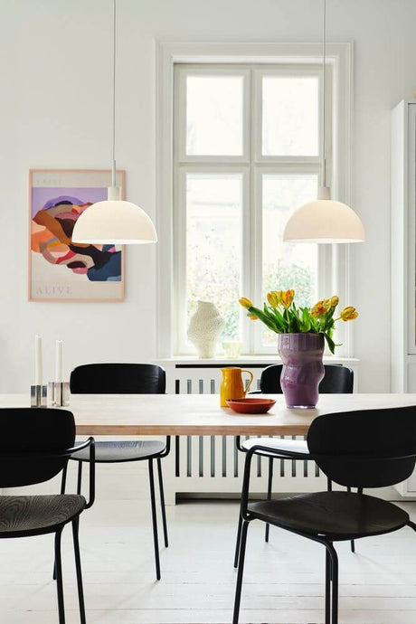 Ellen 30 pendant light above a modern dining table with light-colored flowers and stylish chairs.