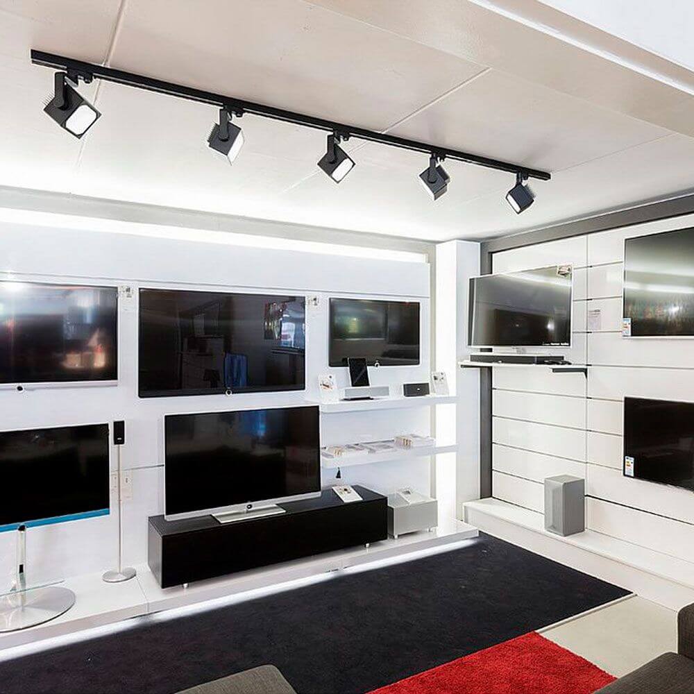 Modernes Verkaufsdisplay mit Euro Cube LED Spot, drei LED-Strahlern an einer Hochvolt-Schiene über mehreren Fernsehern.