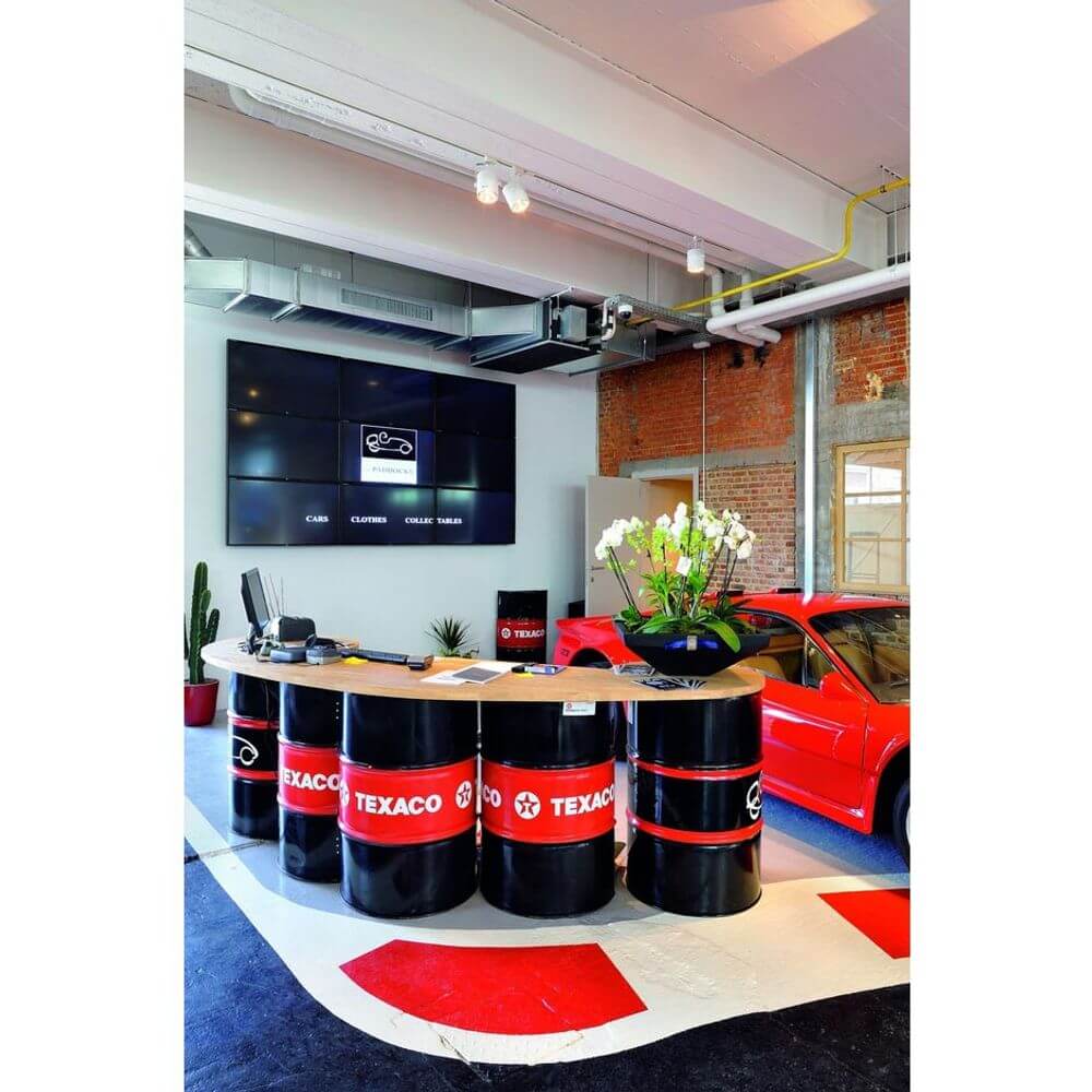 Texaco-tematisert resepsjonsområde med rund disk av oljefat, moderne TV og rød bil.